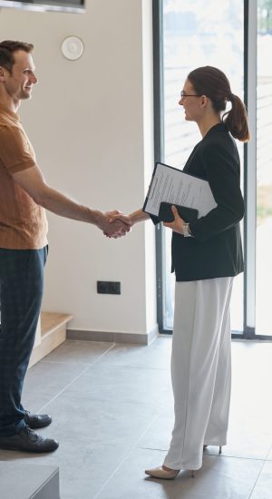 Side view portrait of female real estate agent shaking hands with client during apartment tour, copy space